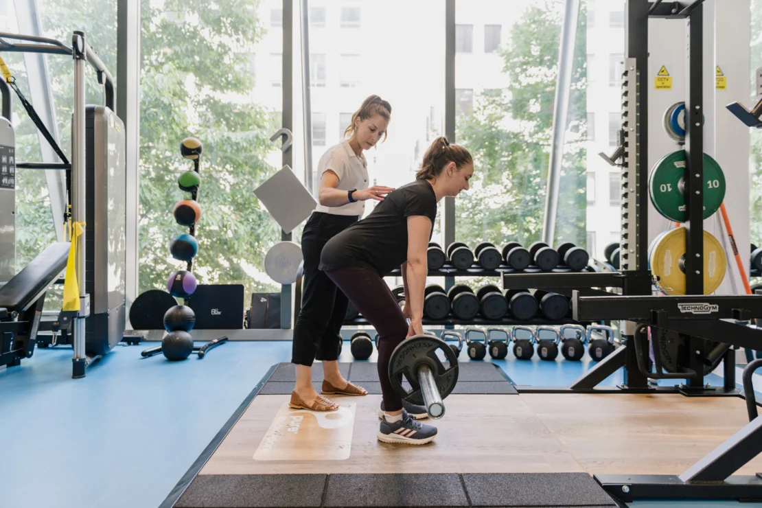 Entrenadora deportiva corrigiendo la técnica de una atleta durante un levantamiento en el gimnasio para prevenir lesiones en HYROX